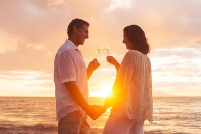 A retired couple is standing on the beach with glasses of champagne