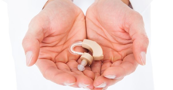 Two hands gently cup a hearing aid