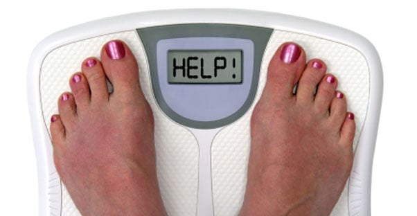The feet of a person are visible on a digital scale that says the world HELP.