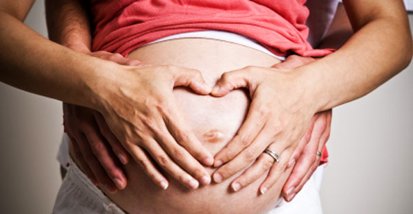 a woman holds her hands on her pregnant belly as she ponders an amniocentesis