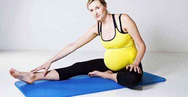 A pregnant woman stretches to touch her feet while doing yoga.