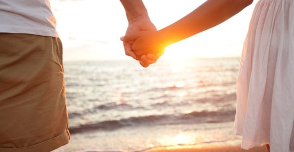 a honeymooning couple holding hands on the beach in front of the sunset