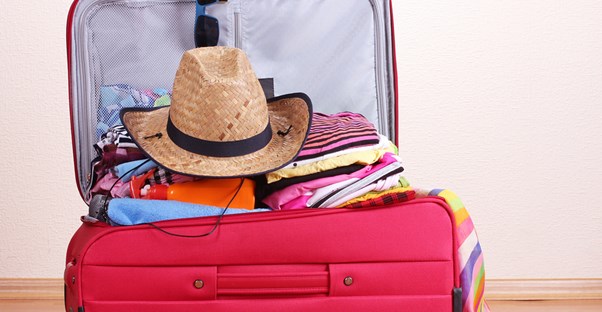a suitcase overflows with closes and a cowboy hat