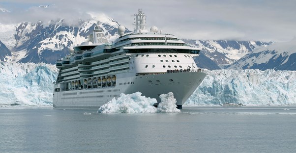 a large cruise ships sails in front of a glacier