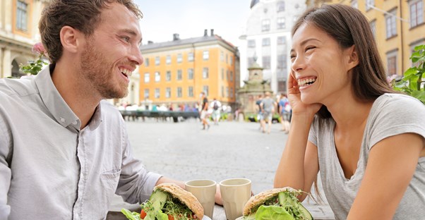 A young laughing couple enjoys their vegan meal in a European city square.