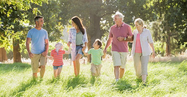 A family of children, parents, and grandparents holds hands while walking through a field.