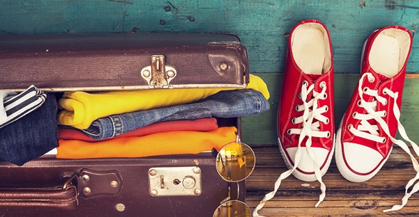 A suitcase is packed completely full next to a pair of red shoes.