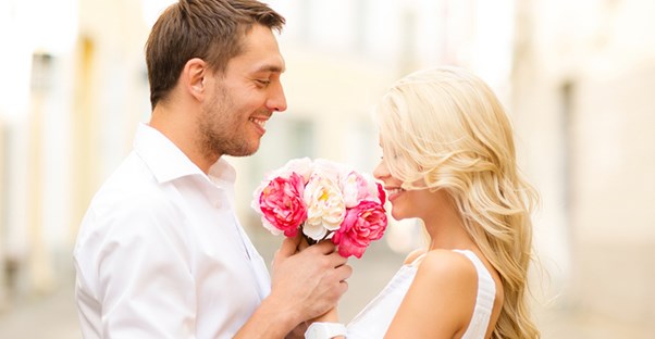 A young couple embraces holding flowers after a successful proposal.