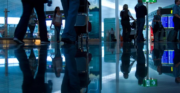 Passengers walk through a busy airport concourse toward airport security.