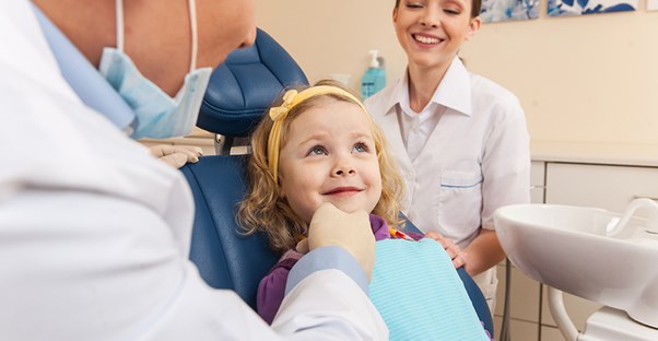 Young girl sitting in dentist chair with dentist and hygienist nearby
