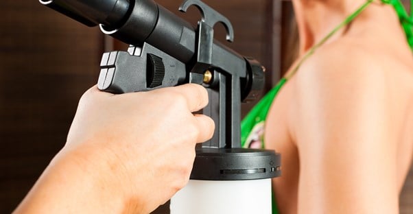 Up close photo of a spray tan gun spraying a woman's shoulder