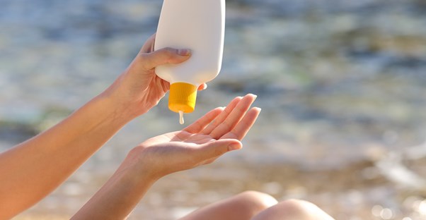 a woman squirts sunscreen into her hand at the beach