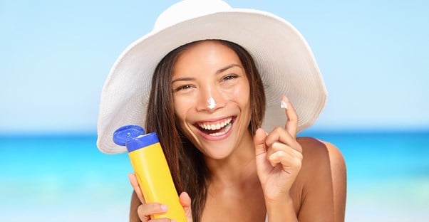 a woman puts sunscreen on her nose while at the beach