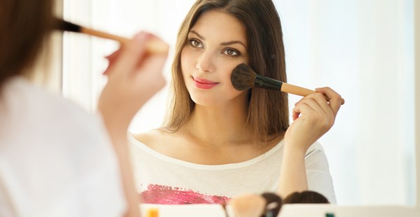 a woman applies makeup to her cheeks in the mirror