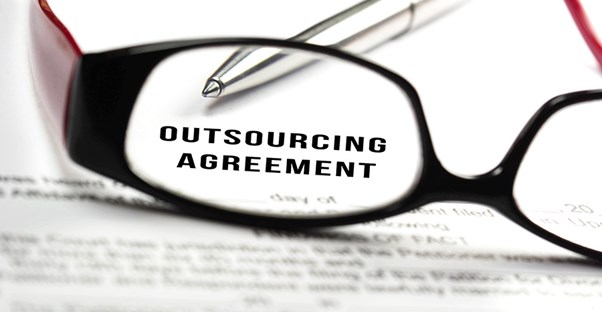 glasses and pen on top of outsourcing agreement contract