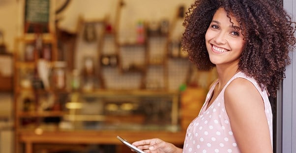 a young woman holding an iPad and smiling at the camera as she stands in front of her small business for which she got a type of business grant