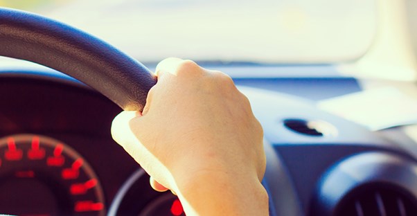 hand on steering wheel of car driving down the road