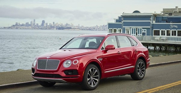 a red 2018 bentley bentayga driving down a road next to the ocean