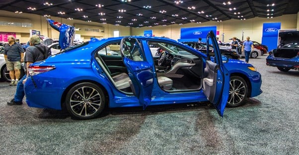 a blue 2019 toyota camry on display with its doors open at an auto show