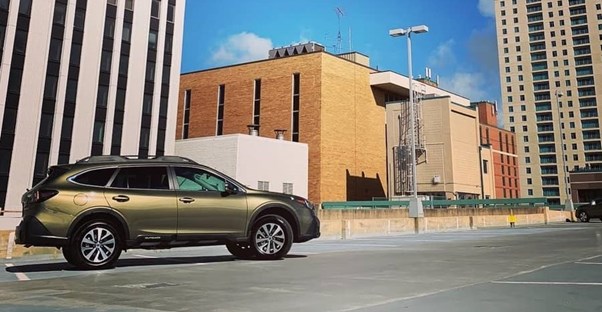 an olive green 2020 subaru outback parked on top of a parking deck in a city