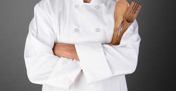 A chef stands with their kitchen utensils