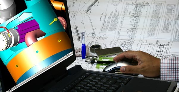 Man working on a mechanical engineering computer program surrounded by design plans.