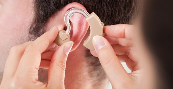 Audiologist places a hearing aid on a patient's ear