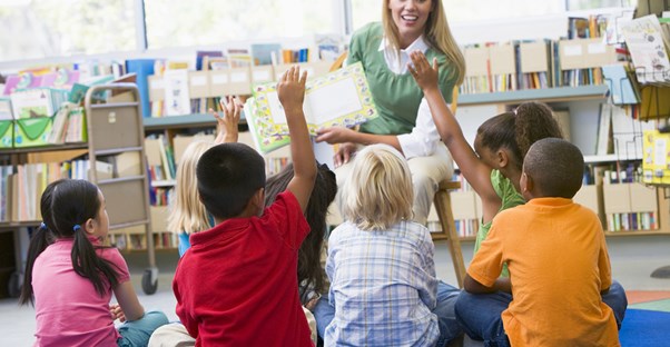 Substitute teacher shows young children a book as children raise their hands