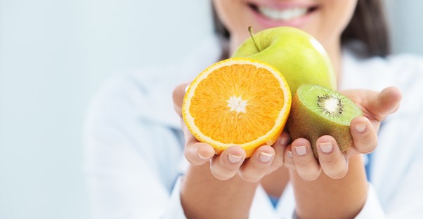 A nutritionist holds up an apple, an orange, and a kiwi