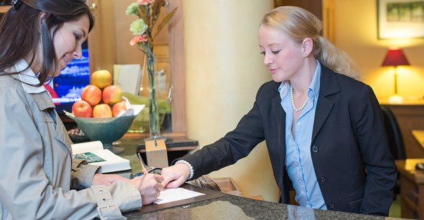 A hospitality manager checks a hotel guest in at the front desk