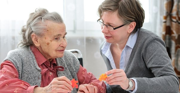 A social worker helps an elderly woman put a puzzle together