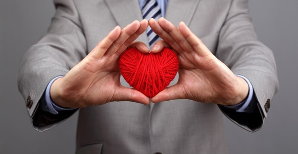 A man in a suit holds up a heart made of yarn