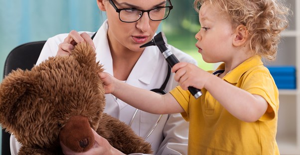 A pediatrician and a little girl play doctor with a stuffed bear