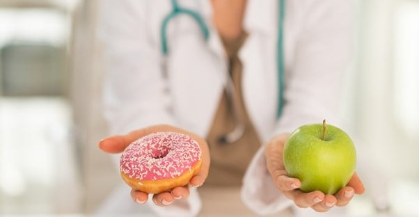 A dietitian holds out an apple and a donut
