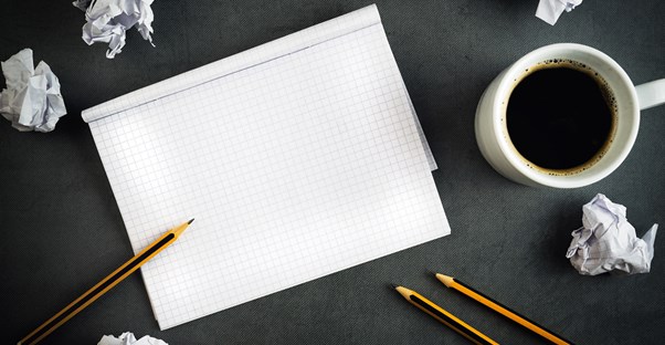A blank notebook on a desk along with pencils and a cup of coffee