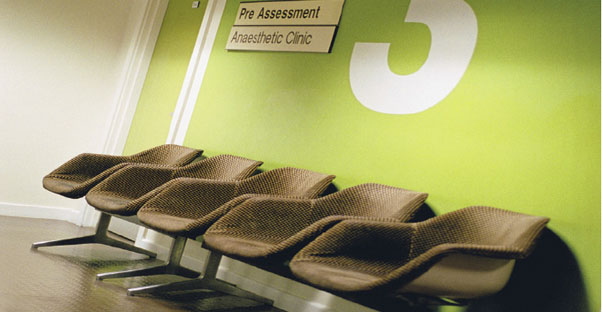 Empty tan chairs located in a green-walled doctors office that says Clinic 3 on the wall.