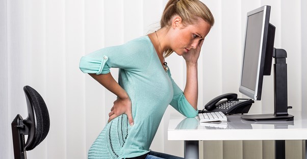 a woman has back pain while sitting at her desk in front of the computer