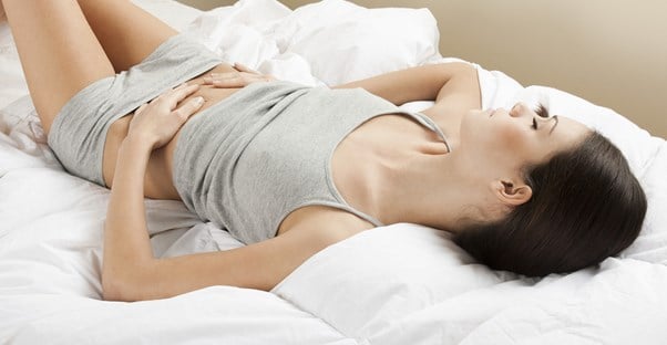 a woman lies on her bed suffering from crohns disease