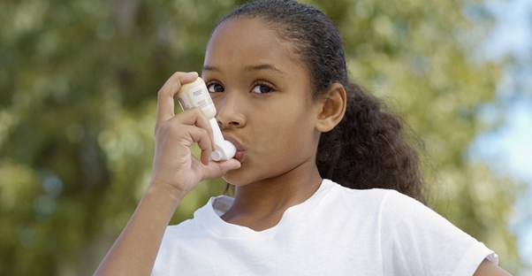 a young girl stops playing to use her inhaler for her asthma