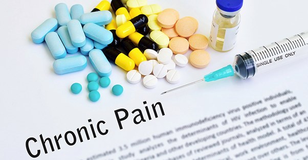 Pills and a syringe are gathered on top of a paper that has a description of chronic pain written on it.