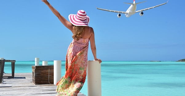 A woman on a pier waves goodbye to a departing plane.