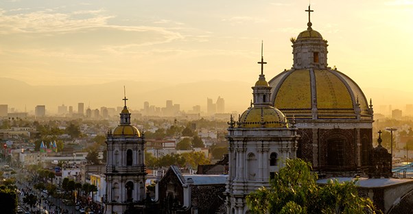 The old building of the Basilica of Our Lady of Guadalupe sits in the foreground of a Mexico City cityscape.