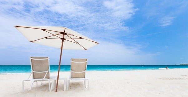 two empty beach chairs undearneath an umbrella on the beach