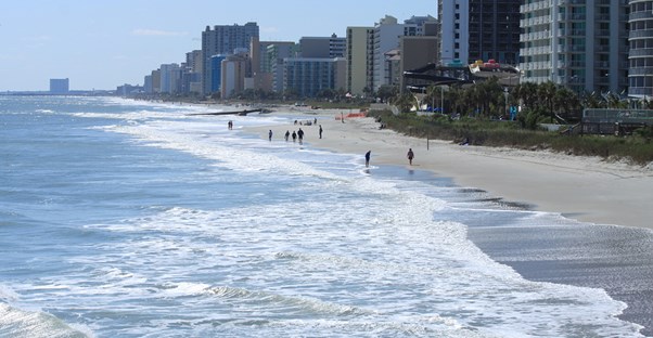 a beach view with high rise hotels and people walking along the shore