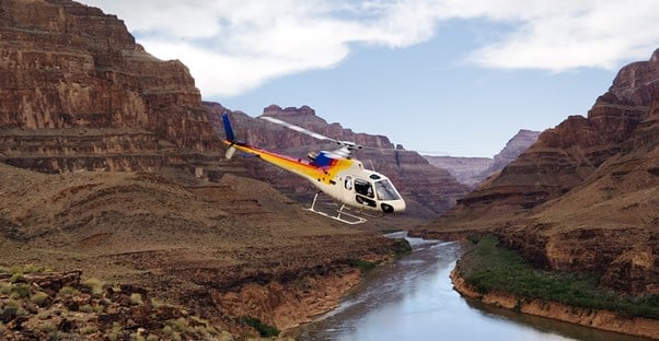 a helicopter flies along the Colorado River through the Grand Canyon