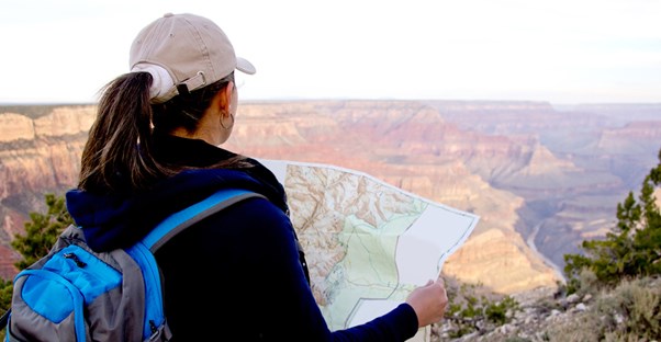 a female hiker examines her map while standing on the edge of the Grand Canyon