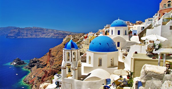 the famous white-washed, blue-roofed building of Santorini sit near the ocean