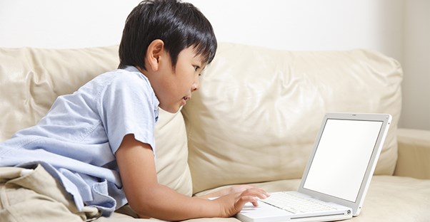 Boy sitting on couch playing on laptop computer