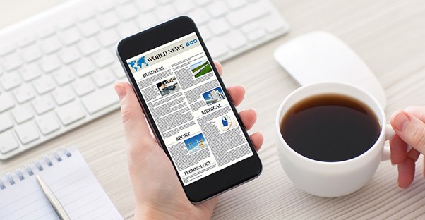 Person drinking cup of coffee and looking at news on smartphone