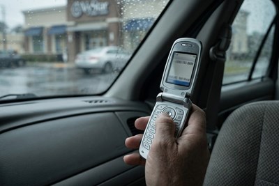 a hand holding a flip cell phone in a car